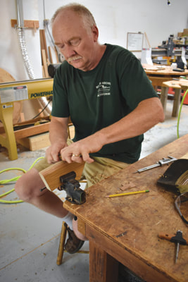 Bob Fuller at work bench sanding a teak wooden steering wheel component in the south shore boatworks wood shop