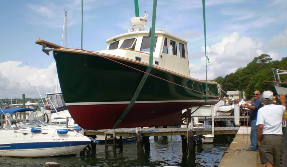 downeast style boat restored and refit by south shore boatworks hanging in slings as it is being dropped back into the water of the ocean
