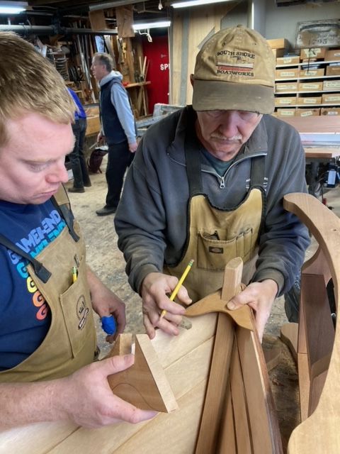 Bob Fuller and student in a wood boat shop fitting the breast plate onto a wooden boat in a class presented by south shore boatworks