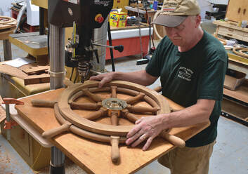 Final fitting of wooden ship yacht wheel by Bob Fuller of South Shore Boatworks on shop bench with chromed bronze hub and teak construction