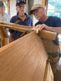 Bob Fuller standing at transom of a wooden boat in his shop teaching a class on wooden boatbuilding