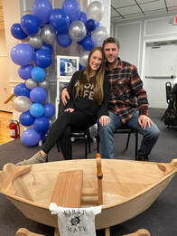a married couple next to their plymouth rock'r wooden rocking boat that will be used for their baby or child that was built in a class offered by bob fuller and south shore boatworks