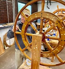 Bob fuller varnishing a traditional wooden yacht ship steering wheel in the south shore boatworks wood shop