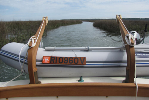 wood and bronze power boat davits built by south shore boatworks with inflatable dinghy secured with ropes wooden teak