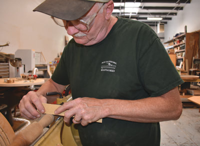 Master Craftsman Bob Fuller of South Shore Boatworks measuring a wooden wheel spoke while on the lathe in the South Shore Boatworks wood shop