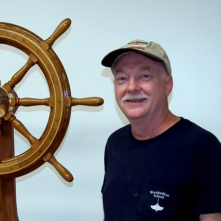 Bob fuller of south shore boatworks portrait next to varnished wooden traditional ship or yacht steering wheel