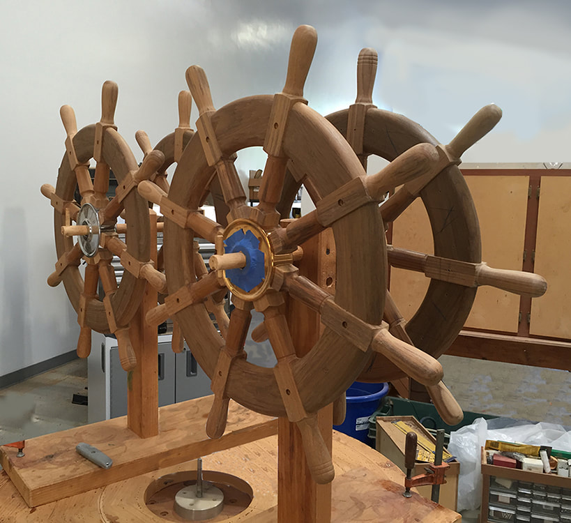 wooden traditional boat and yacht steering wheels on stands in the south shore boatworks shop awaiting varnish with bronze hubs and wooden handles